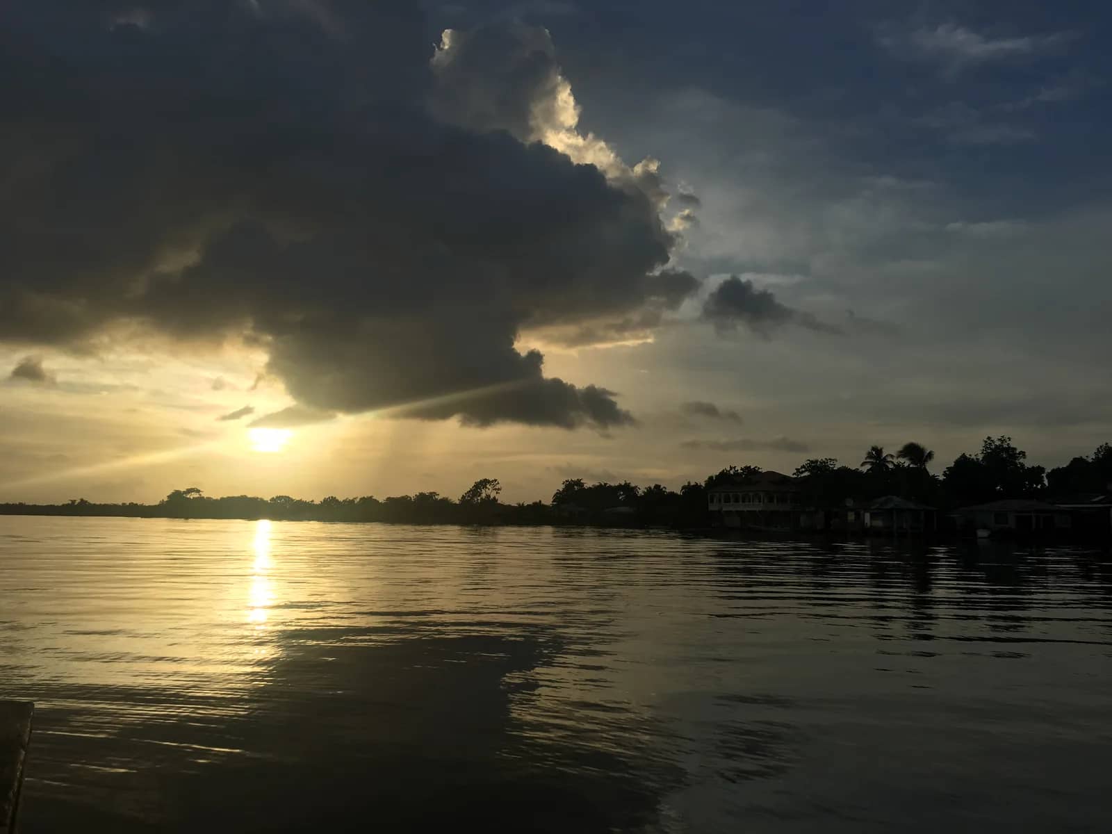 Sunset over a river with dark clouds above the shoreline