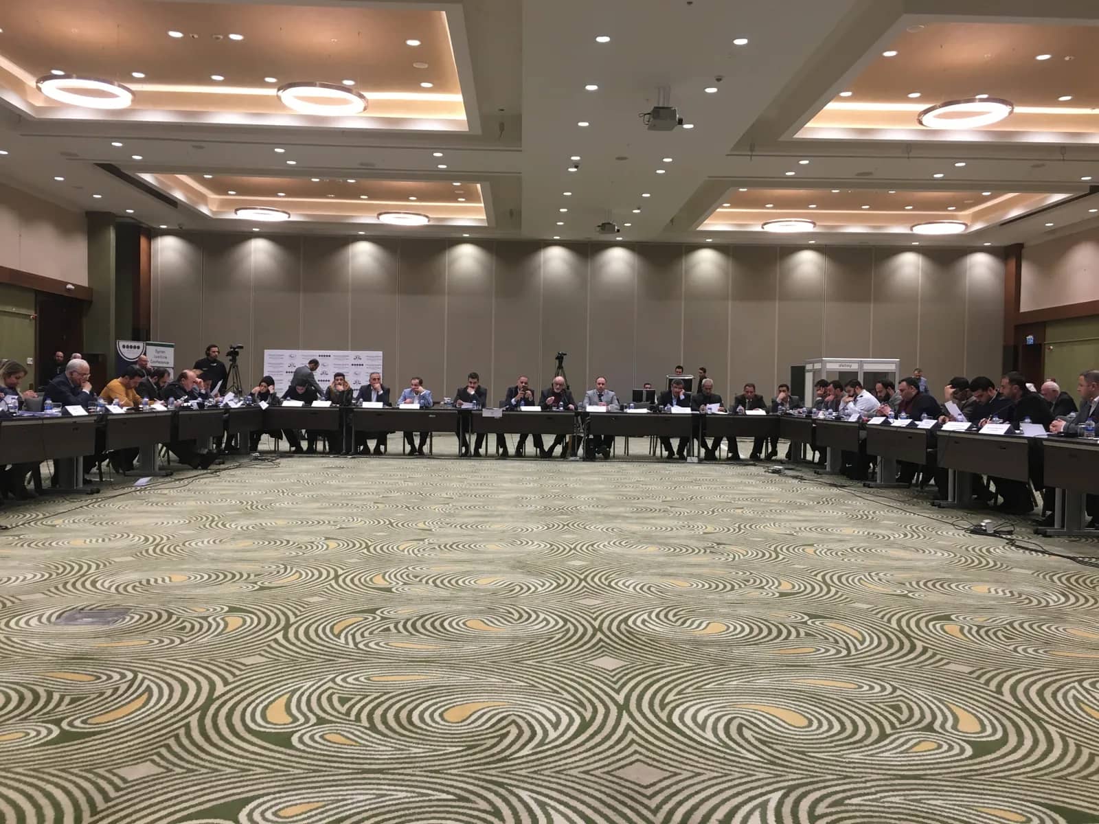 Conference participants seated around tables in a large meeting room